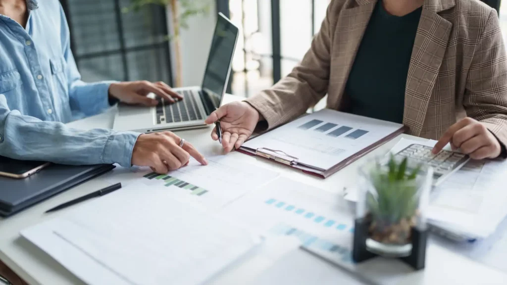 Due professionisti analizzano insieme report finanziari, grafici e un piano di cassa durante una consulenza aziendale
