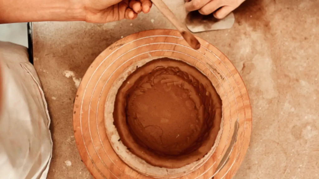 Due persone modellano insieme un vaso di argilla al tornio: l'apprendimento del mestiere accanto a chi sa già farlo.